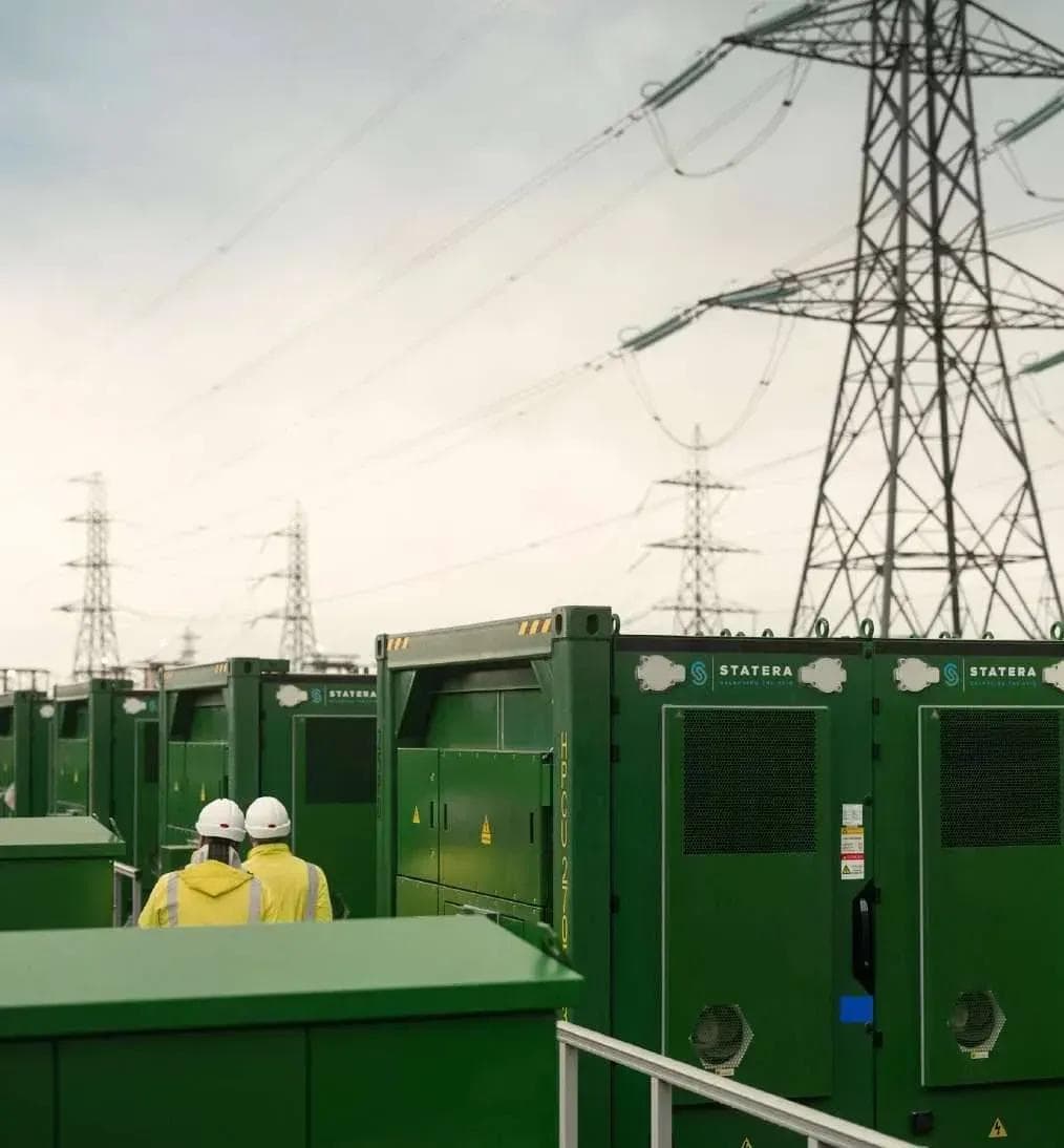 Two workers beside power equipment under transmission towers